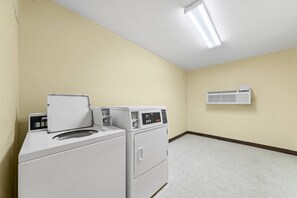 A laundry room with two front-loading washers and dryers, a wall-mounted heater, and a light fixture on the ceiling.