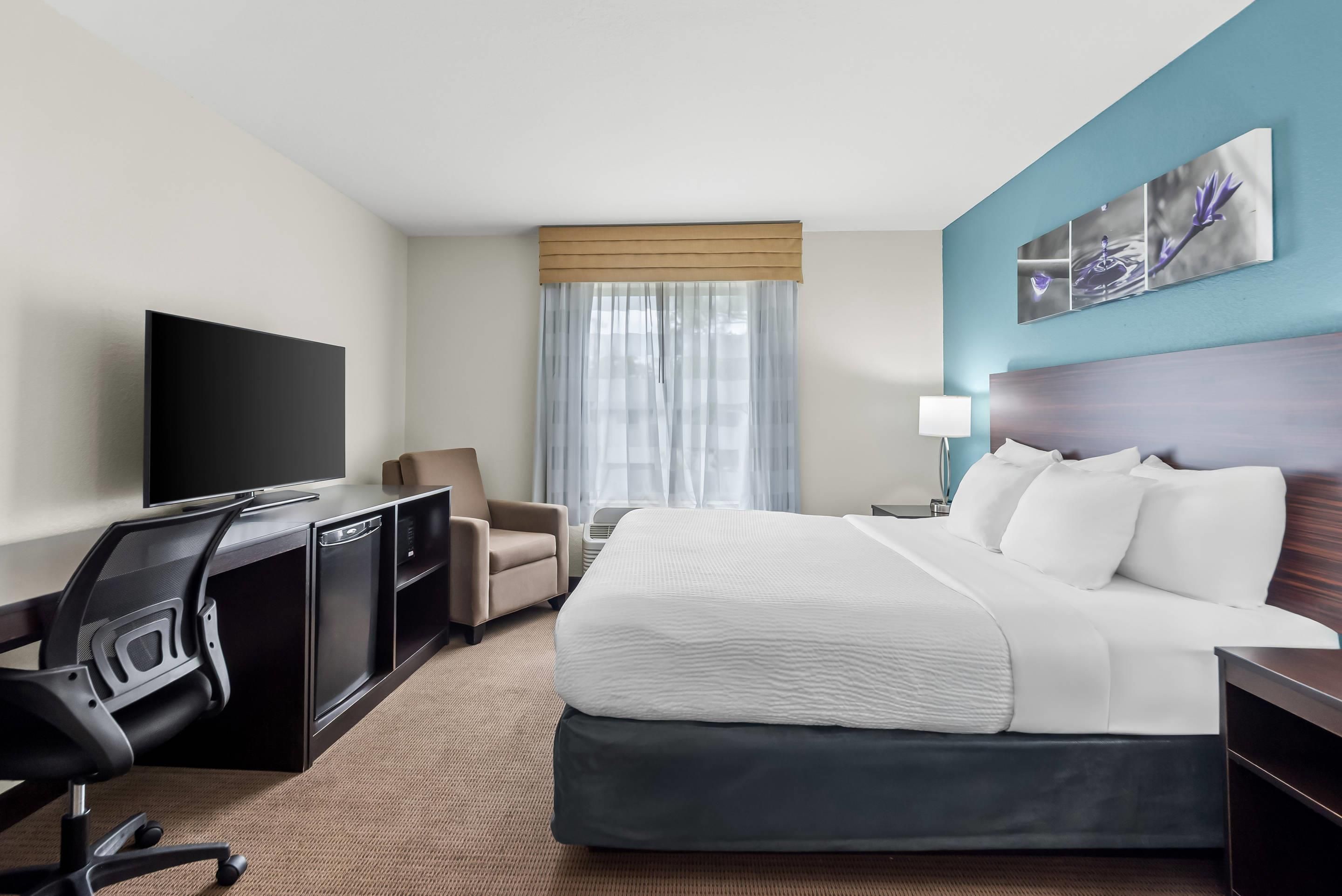 Una habitación de hotel con cama, escritorio con silla, televisor y ventana con cortinas.