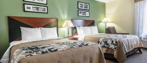 Habitación de hotel con dos camas, cada una con cabecero de madera, colcha con motivos florales y mesita de noche con lámpara. En la pared hay cuadros enmarcados y una ventana con cortinas.