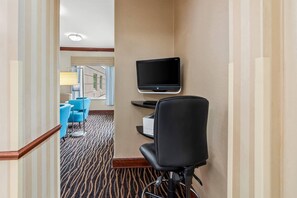 A hotel room with a television mounted on the wall, a desk with a printer, and a chair.