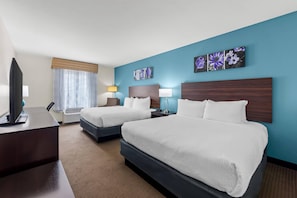 A hotel room with two beds, a desk, a TV, and artwork on the walls.
