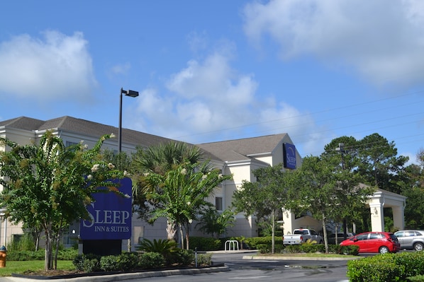 Edificio de Sleep Inn & Suites con un letrero, rodeado de palmeras y automóviles estacionados.