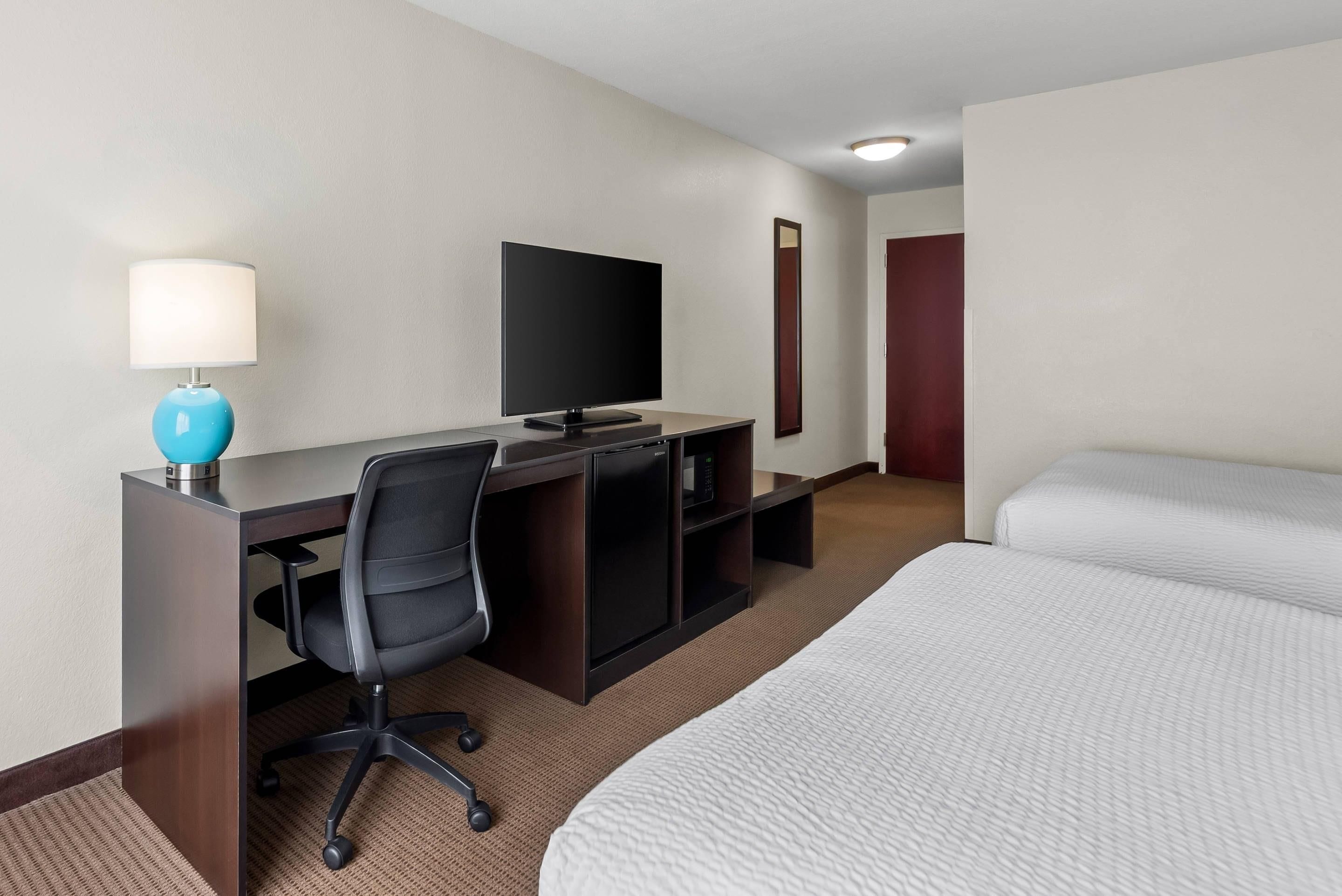 Una habitación de hotel con cama, escritorio con computadora, silla, televisor y microondas.