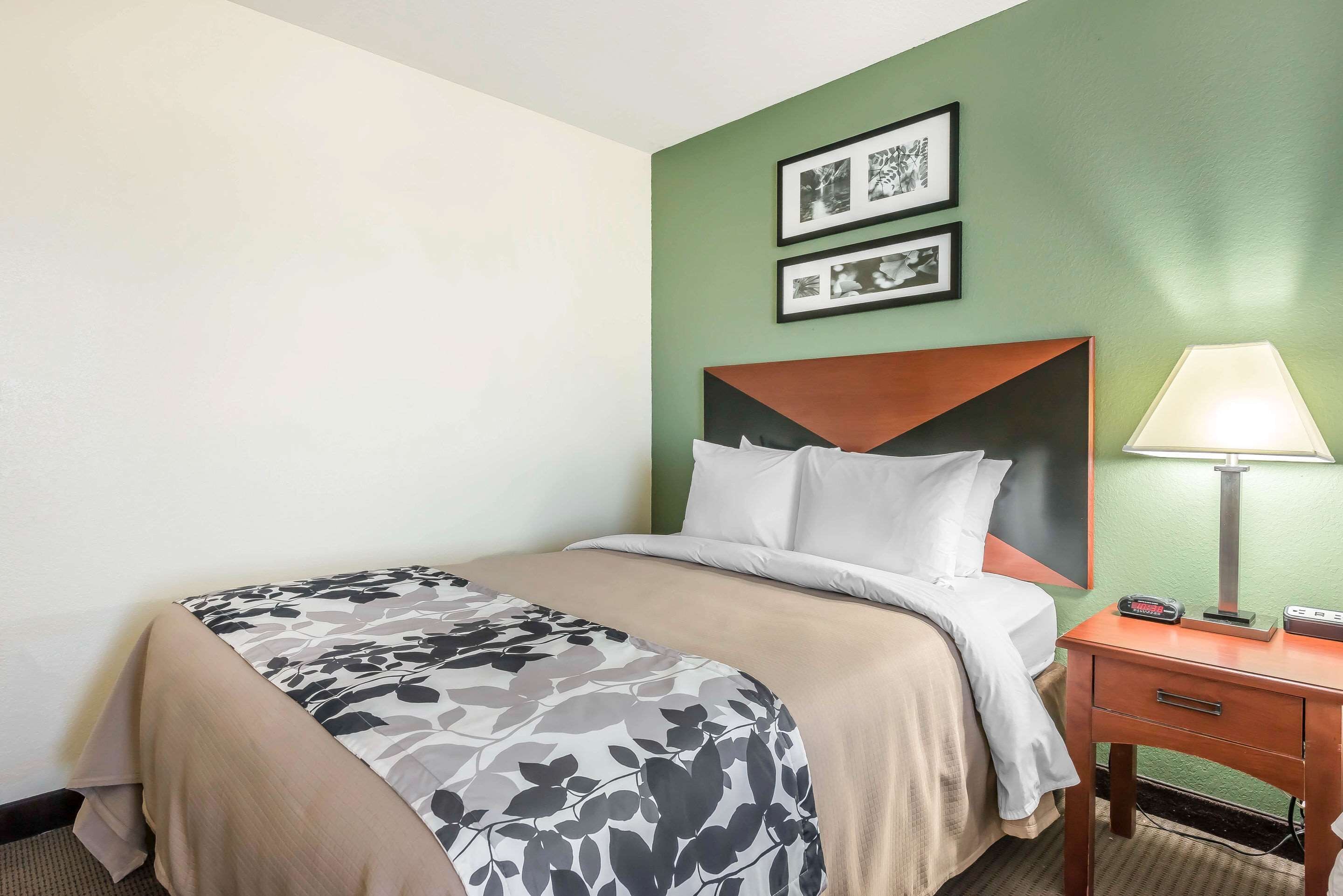 A hotel room with a bed, a nightstand with a lamp, and two framed pictures on the wall.