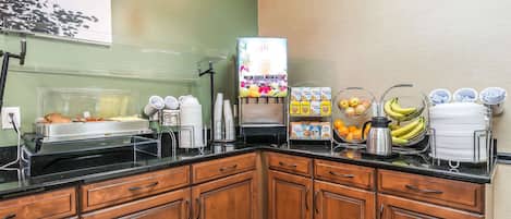 A breakfast bar with a juice dispenser, cereal boxes, and fruit bowls.