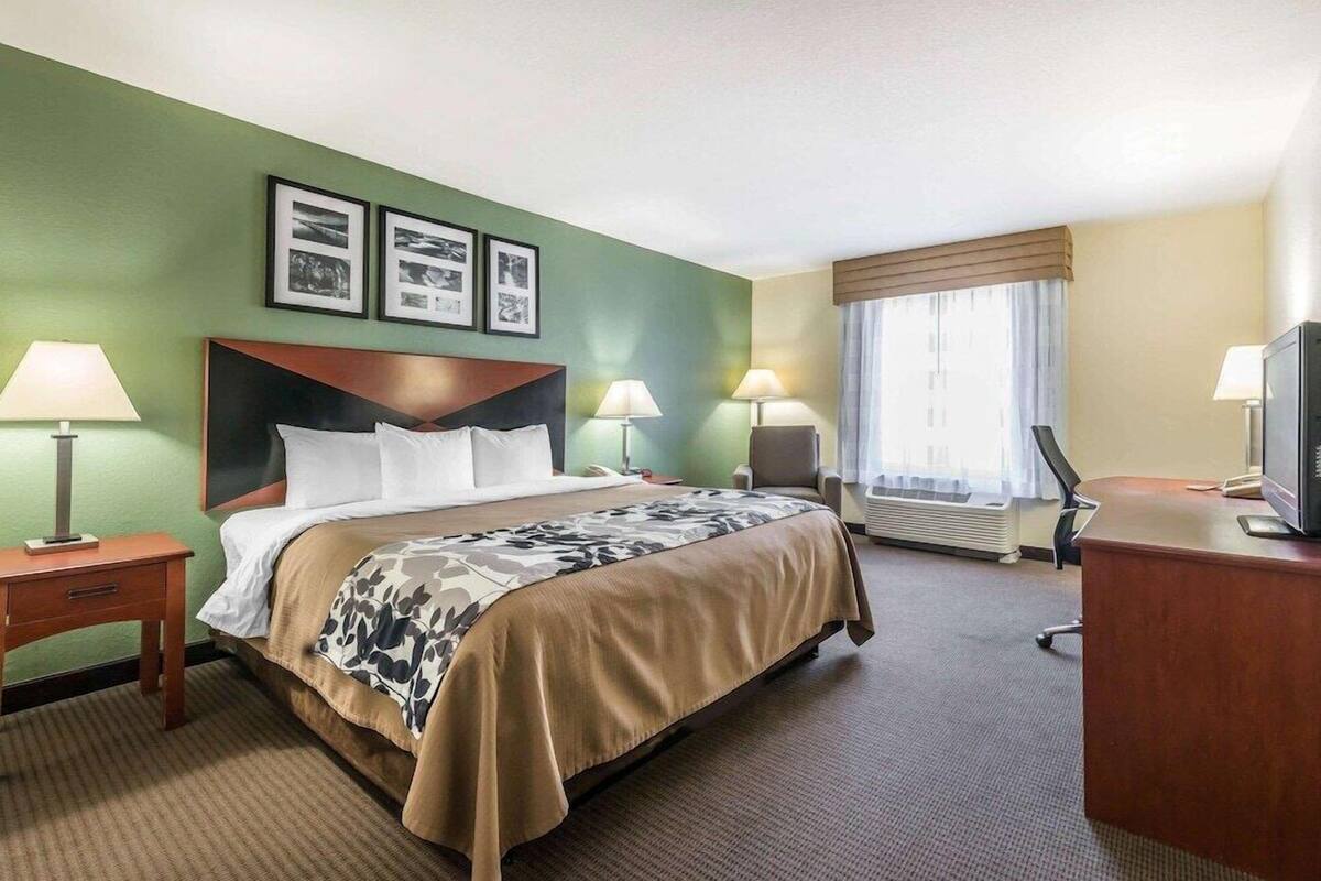 Une chambre d’hôtel comprenant un lit, deux tables de chevet avec des lampes, un bureau avec une télévision et une fenêtre avec des rideaux.