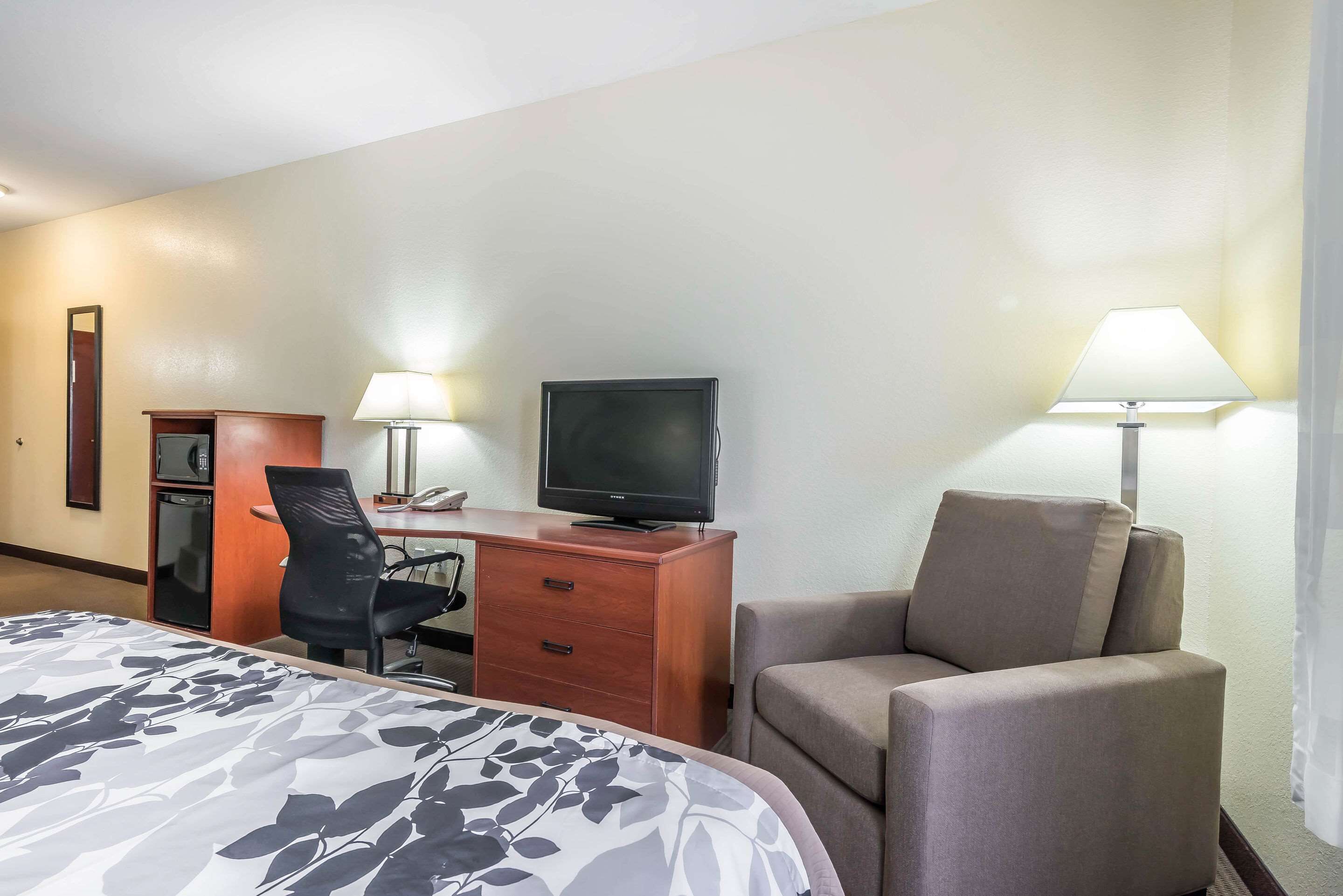 Una habitación de hotel con una cama, un escritorio con computadora, televisión, una silla y una lámpara.