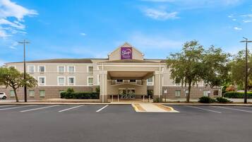 Un hotel con techo plano, entrada central y estacionamiento al frente.