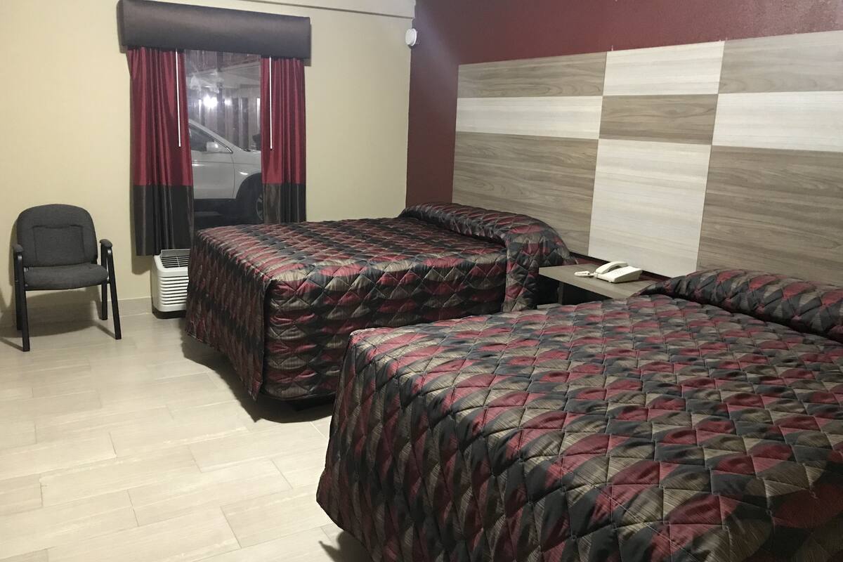 A hotel room with two beds, a chair, a small table, and a phone.