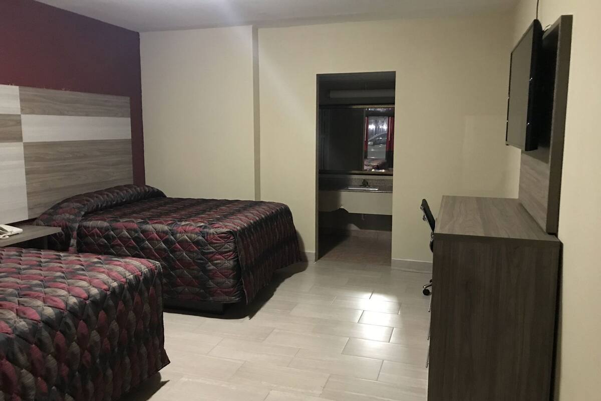 A room with two beds, a desk, a mirror, a TV, and a small kitchenette.