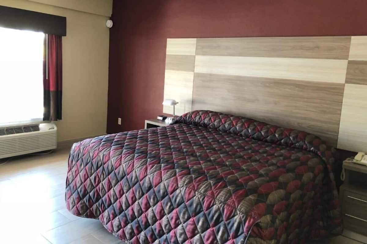 A bedroom with a large bed, a nightstand, a lamp, and a window with curtains.