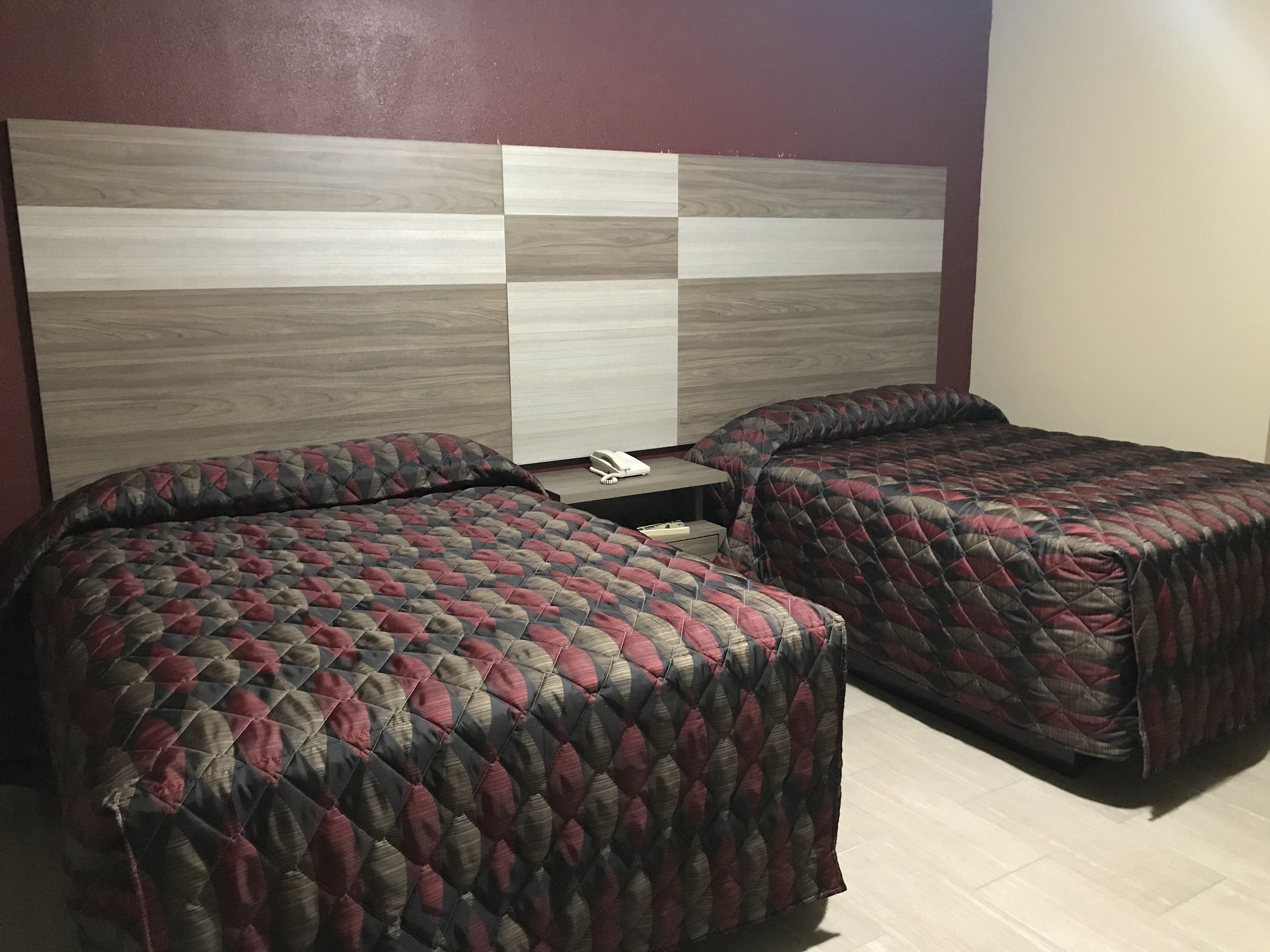 Habitación de hotel con dos camas, cabecera de madera y mesita de noche con teléfono.