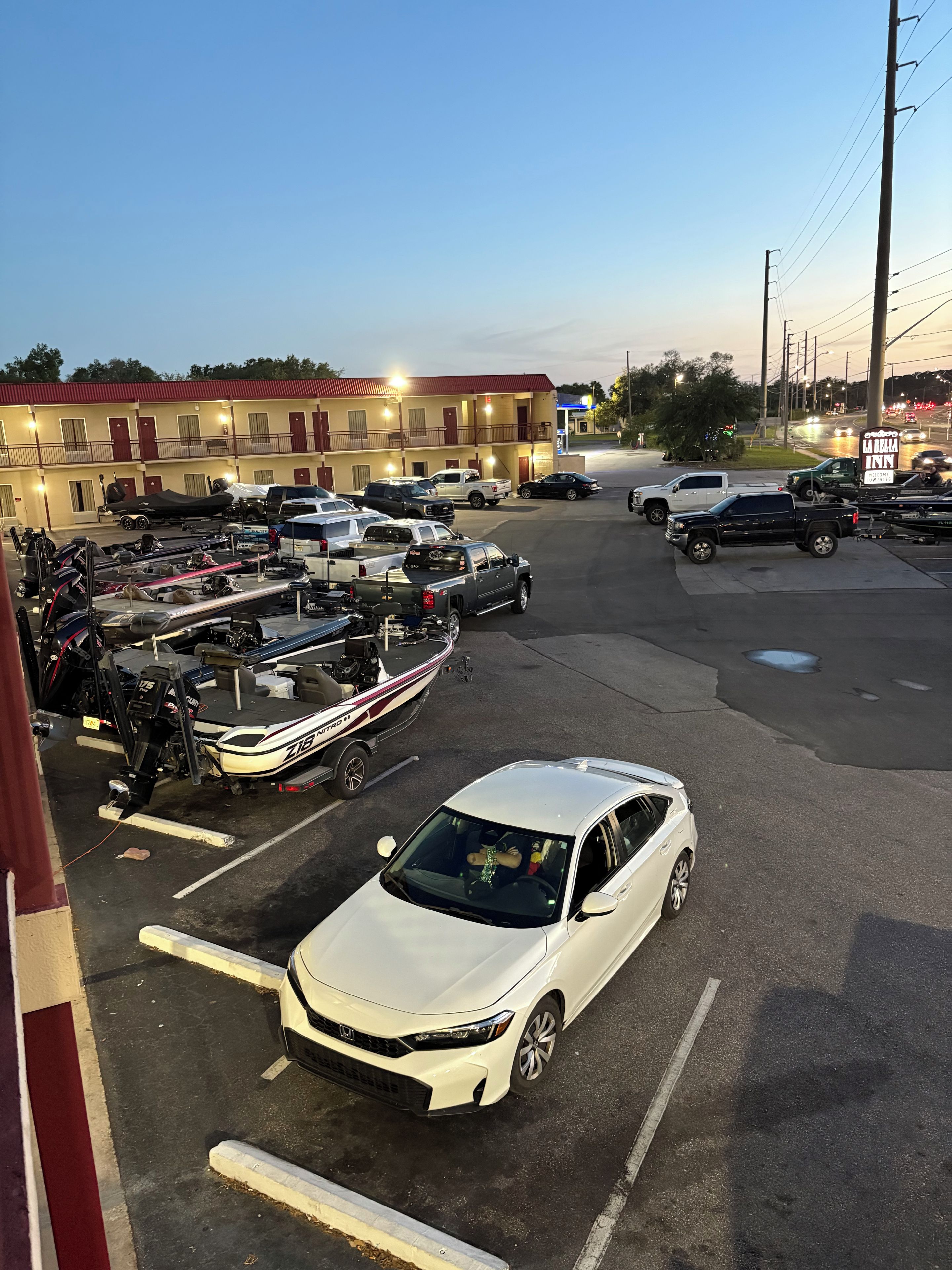 A parking lot with multiple vehicles, including a white car, and a building with a red roof in the background.