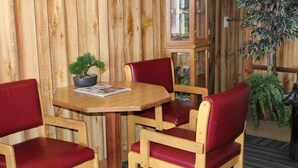 A wooden interior with a round table, red cushioned chairs, a potted plant, and a cabinet with glass doors. - Ontario Inn (Ontario)
