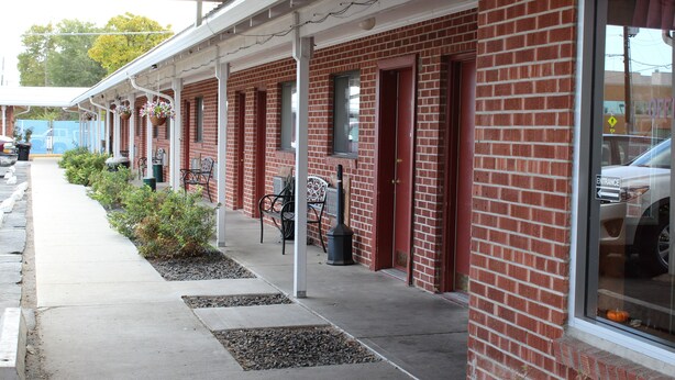 A row of brick buildings with a covered walkway, outdoor seating, and a visible entrance sign. - Ontario Inn (Ontario)