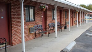 A row of red brick motel rooms with white pillars, outdoor seating, and hanging flower baskets. - Ontario Inn (Ontario)