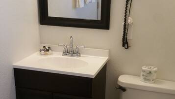 A bathroom with a white sink, dark cabinets, a toilet, a mirror, and a framed picture on the wall.
