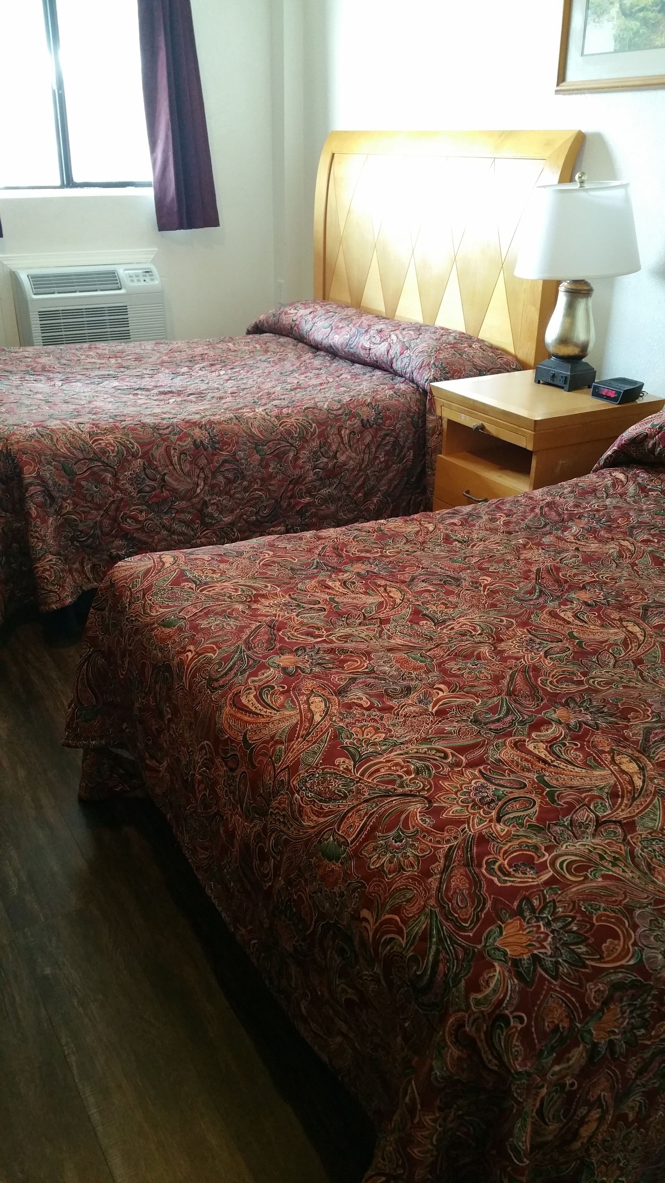 A hotel room with two beds, a nightstand with a lamp, and an air conditioning unit.