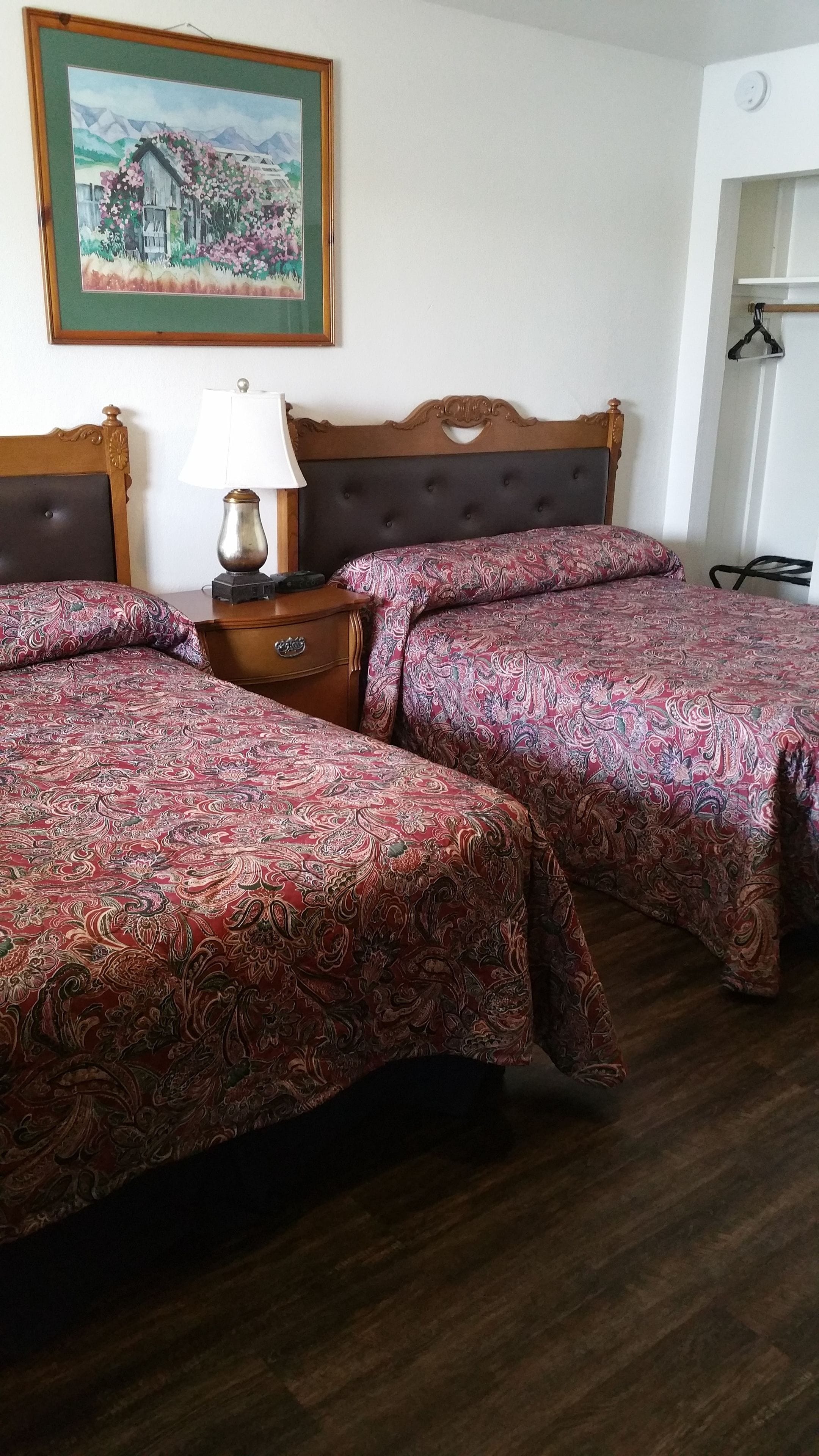A hotel room with two beds, a wooden headboard, a nightstand with a lamp, and a painting on the wall.