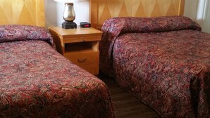 A hotel room with two beds, a wooden headboard, a nightstand with a lamp, and a framed picture on the wall.