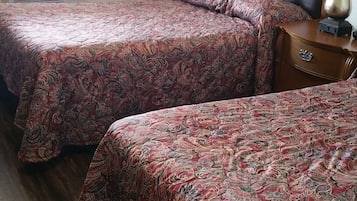 A hotel room with two beds, a wooden headboard, a bedside table with a lamp, and a window with curtains.