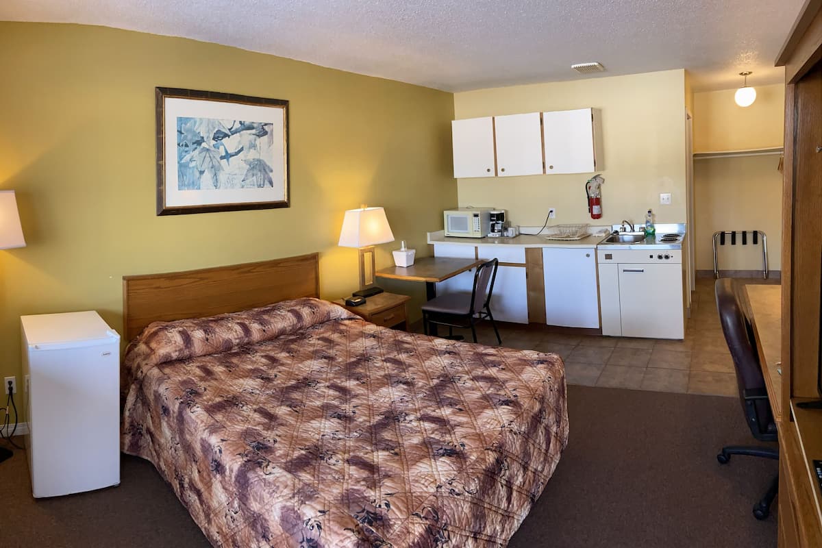 A hotel room with a bed, bedside table, lamp, and a kitchenette area with a microwave, coffee maker, and sink.