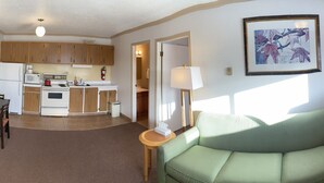 A compact living space with a kitchenette, a television, a sofa, and a window with curtains. - Tumbler Ridge Inn (Tumbler Ridge)