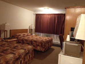 A hotel room with two beds, a desk with a lamp, a television, and a window with curtains.