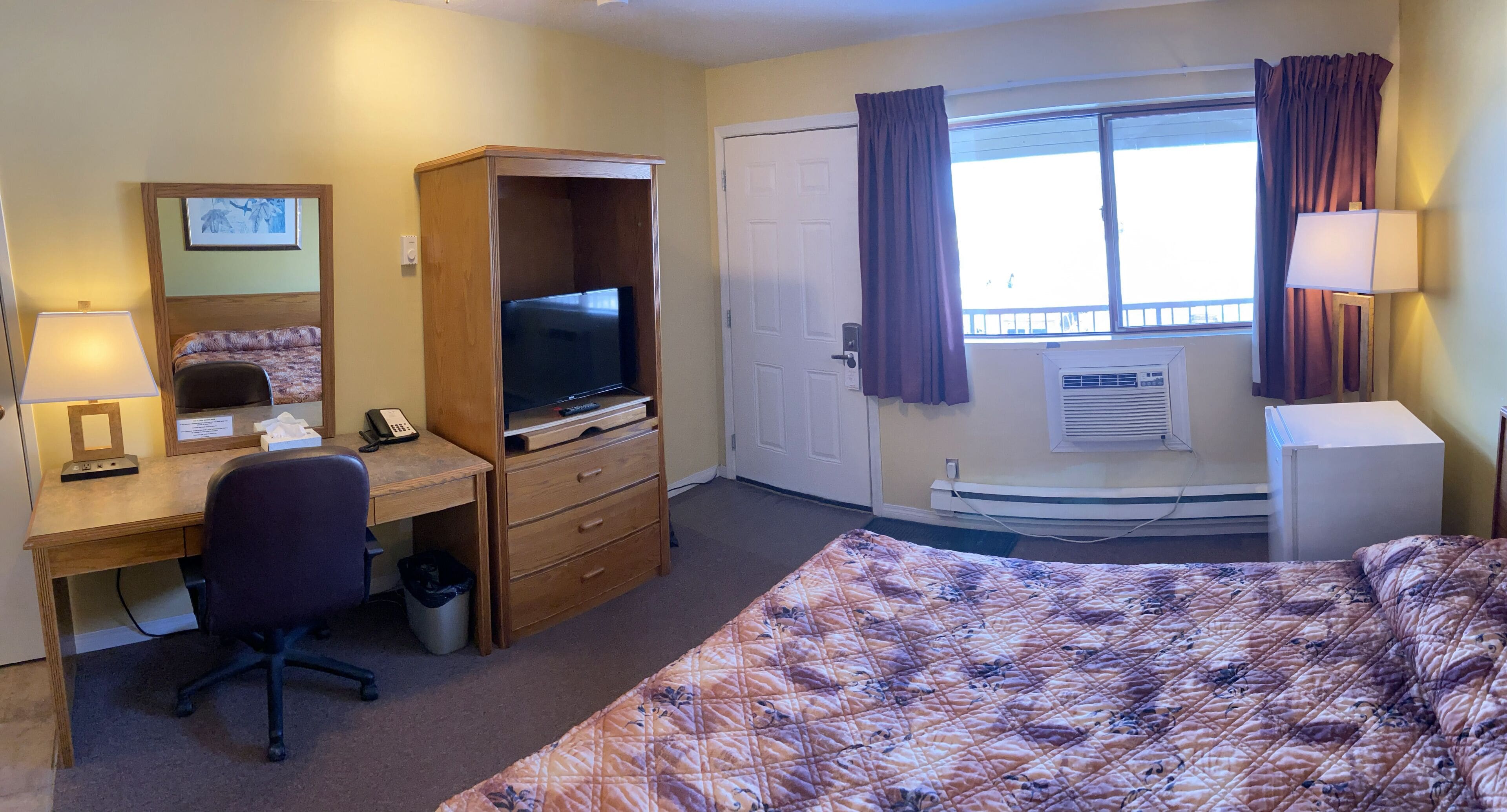 A hotel room with a bed, desk, chair, television, and a window with curtains.