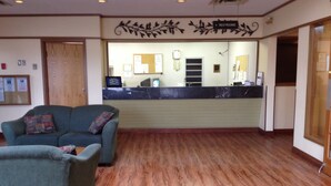 A reception area with a counter, a seating area with two sofas, and a wooden floor. - Tumbler Ridge Inn (Tumbler Ridge)