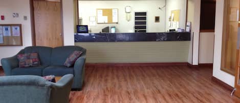 A reception area with a counter, a seating area with two sofas, and a wooden floor.