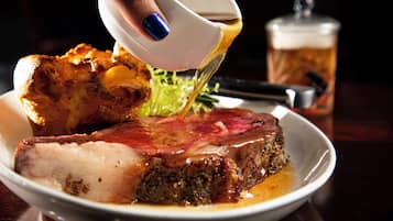 A plate of food with a large piece of meat and vegetables, and a hand pouring sauce over it.
