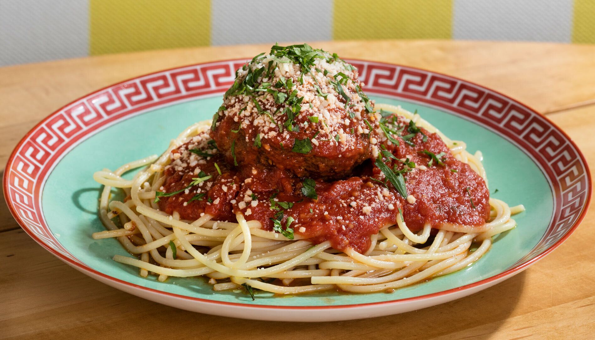 A plate of spaghetti with meatballs and tomato sauce, garnished with herbs and grated cheese.