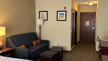 Una habitación de hotel con cama, sofá, escritorio, lámpara y dos cuadros en la pared.