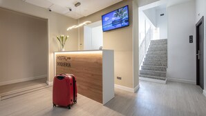A reception desk with a wooden finish, a television mounted above it, and a staircase to the right. - Standbyme Ramblas (Barcelona)