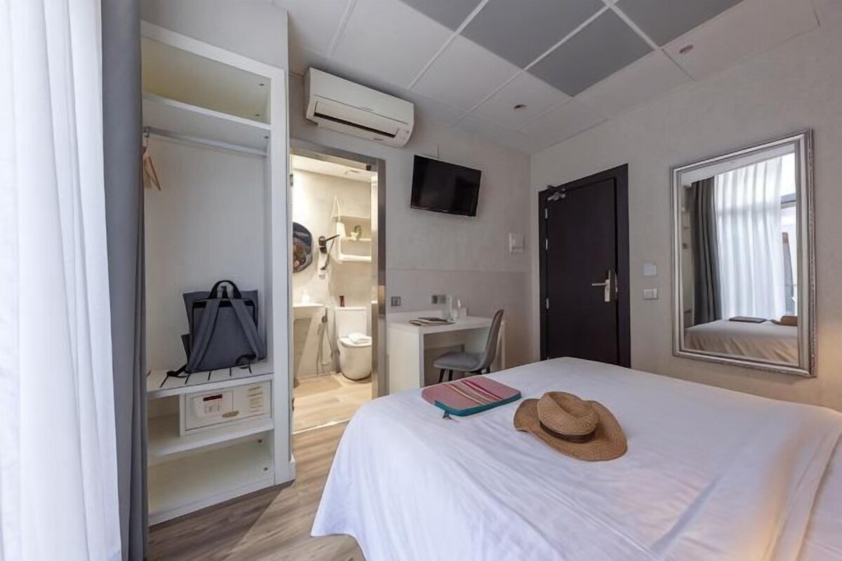 A hotel room with a bed, a desk, a chair, a wardrobe, a TV, and a window.