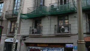 A multi-story building with balconies, a graffiti-covered garage door, and a sign for a hostel. - Standbyme Ramblas (Barcelona)