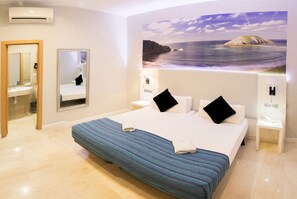 A hotel room with a large bed, a bathroom with a mirror, and a painting of a beach scene on the wall. - Standbyme Ramblas (Barcelona)