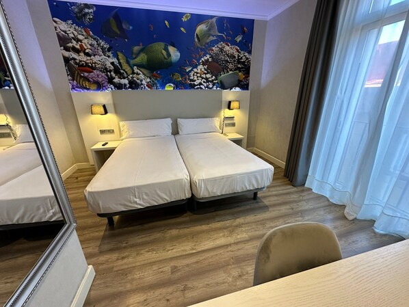 Ein Hotelzimmer mit zwei Betten, einer großen Aquarium-Wand, Holzböden und einem Schreibtisch mit Stuhl.