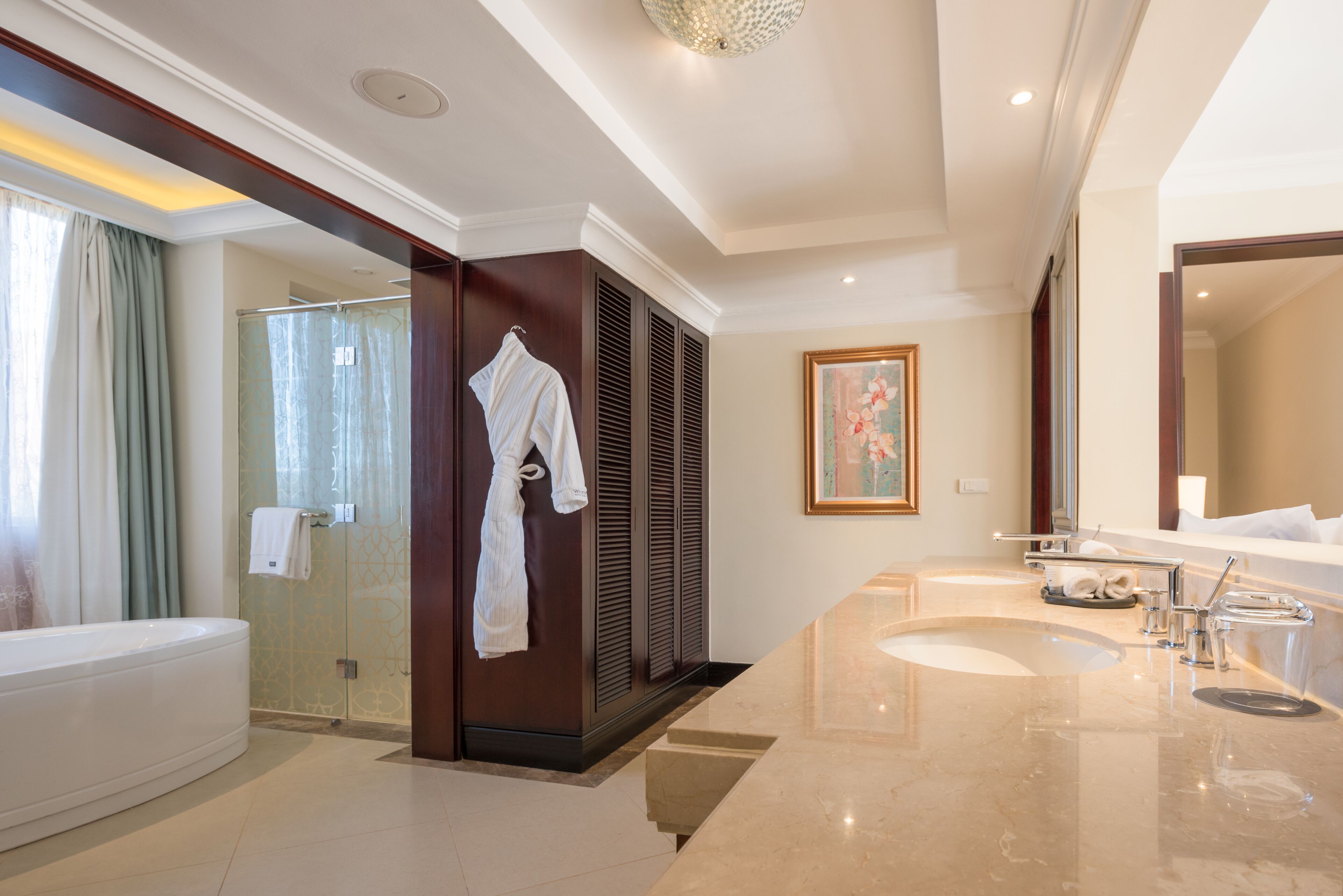 A modern bathroom with a bathtub, a glass shower enclosure, a vanity with a large sink, and a robe hanging on a rack.