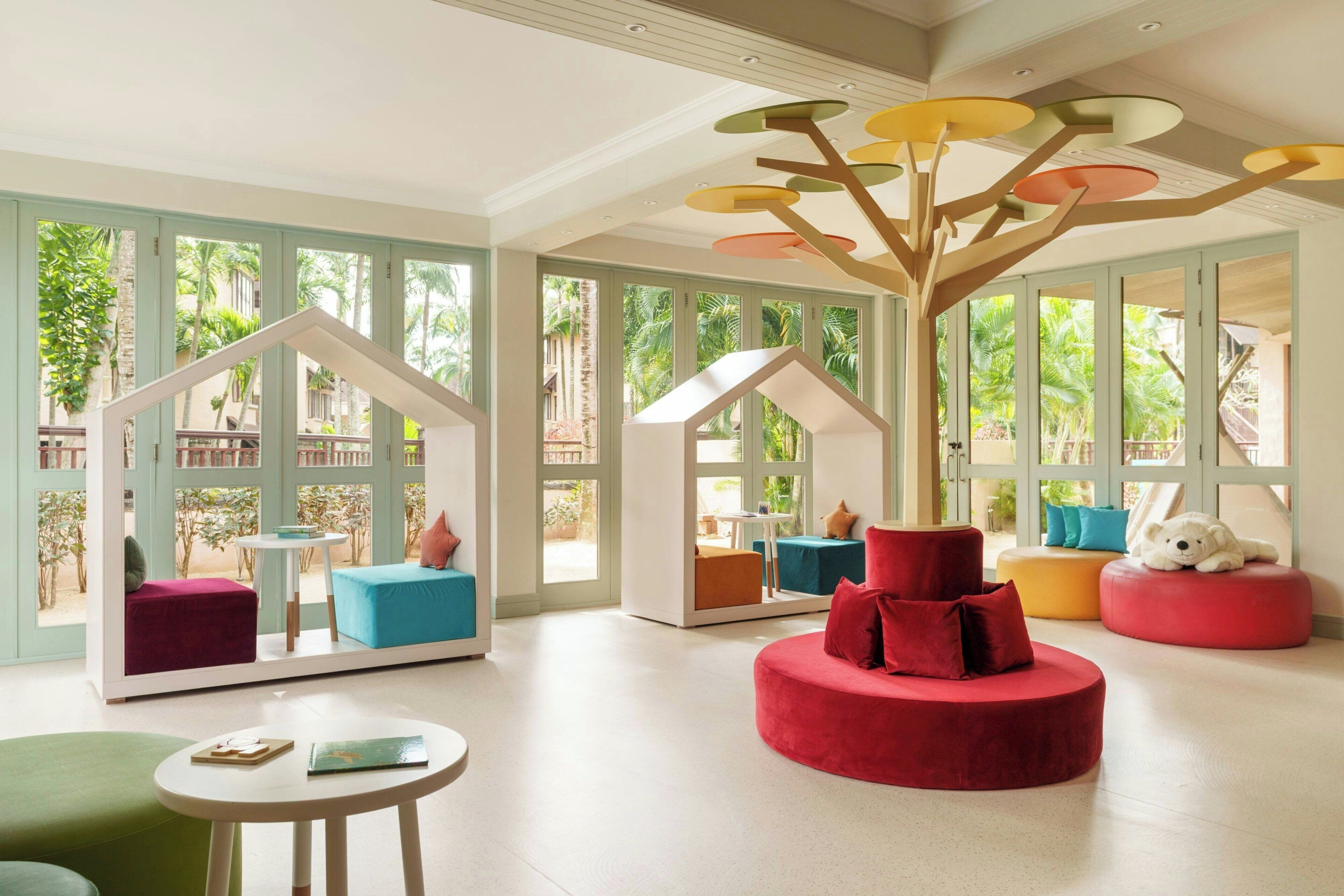 A modern interior with large windows, a central red seating area, and a unique ceiling light fixture.