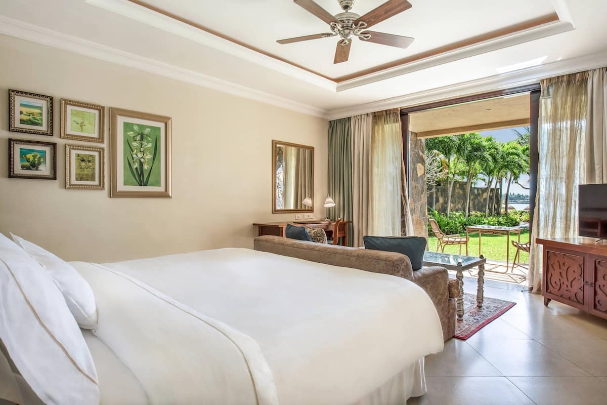 Quarto de hotel com uma cama grande, uma escrivaninha, uma cadeira e varanda com vista para palmeiras.