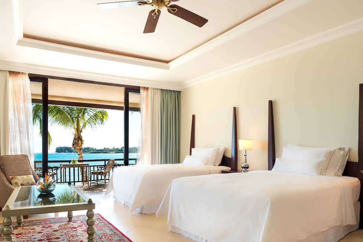Quarto de hotel com duas camas, uma varanda e vista para o mar, e um ventilador de teto.