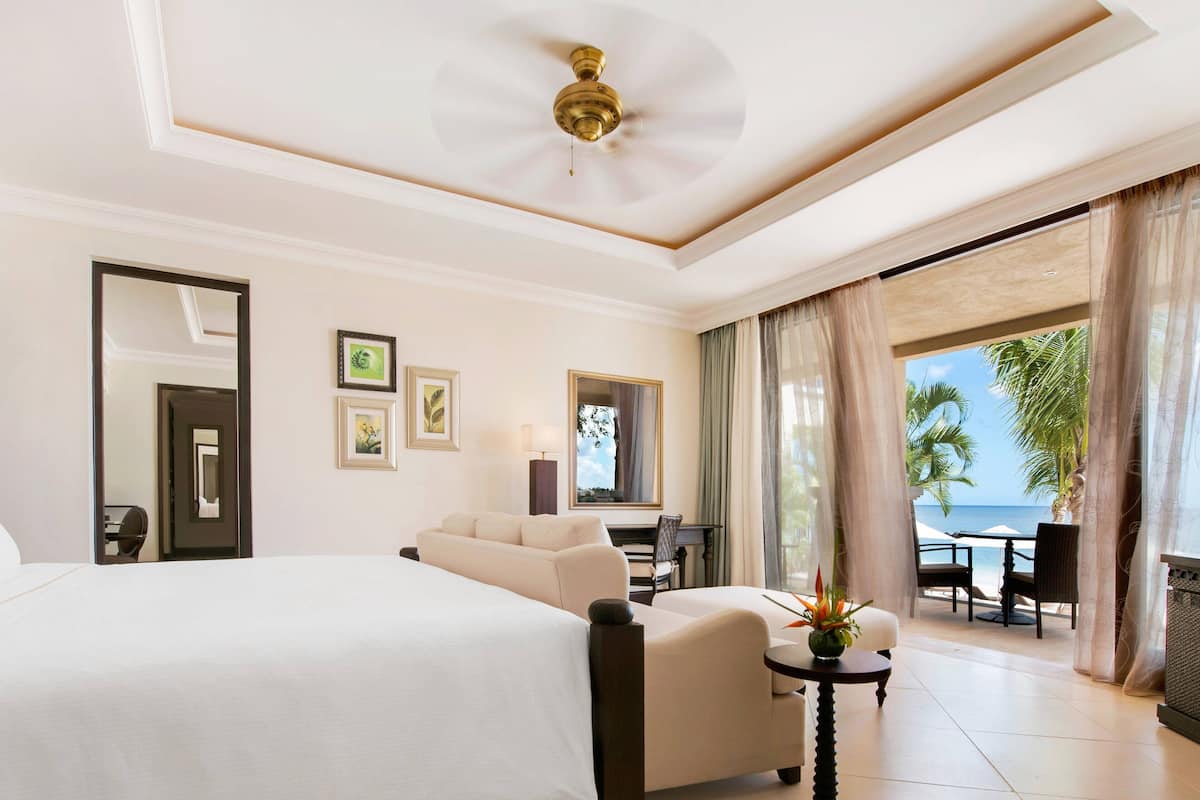 Quarto de hotel com uma cama grande, área de estar com mesa e vista para o oceano.