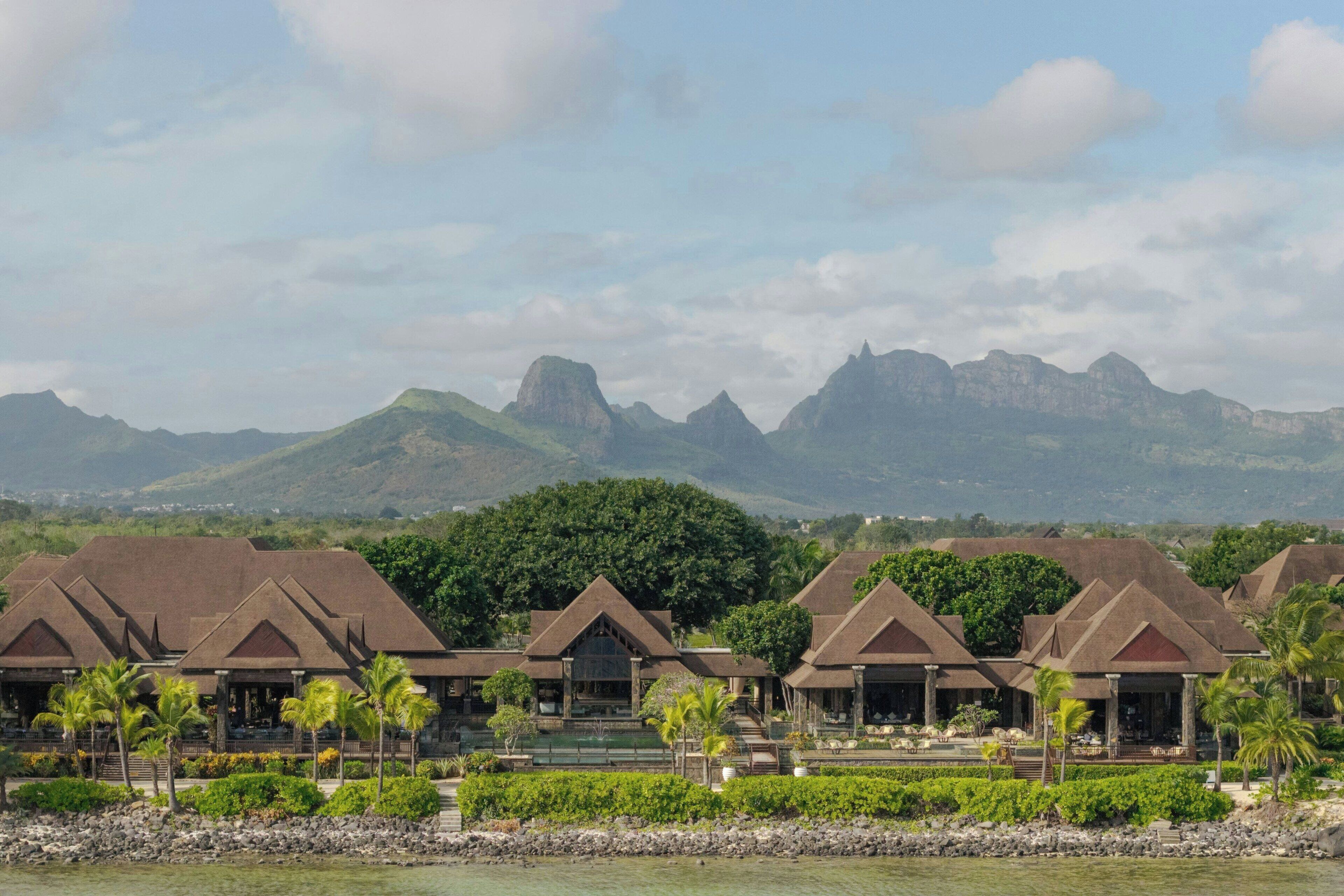 Un resort con varias construcciones tipo bungalow, una costa rocosa y montañas al fondo.