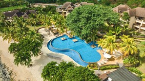 A resort with a large pool, palm trees, and beach access.