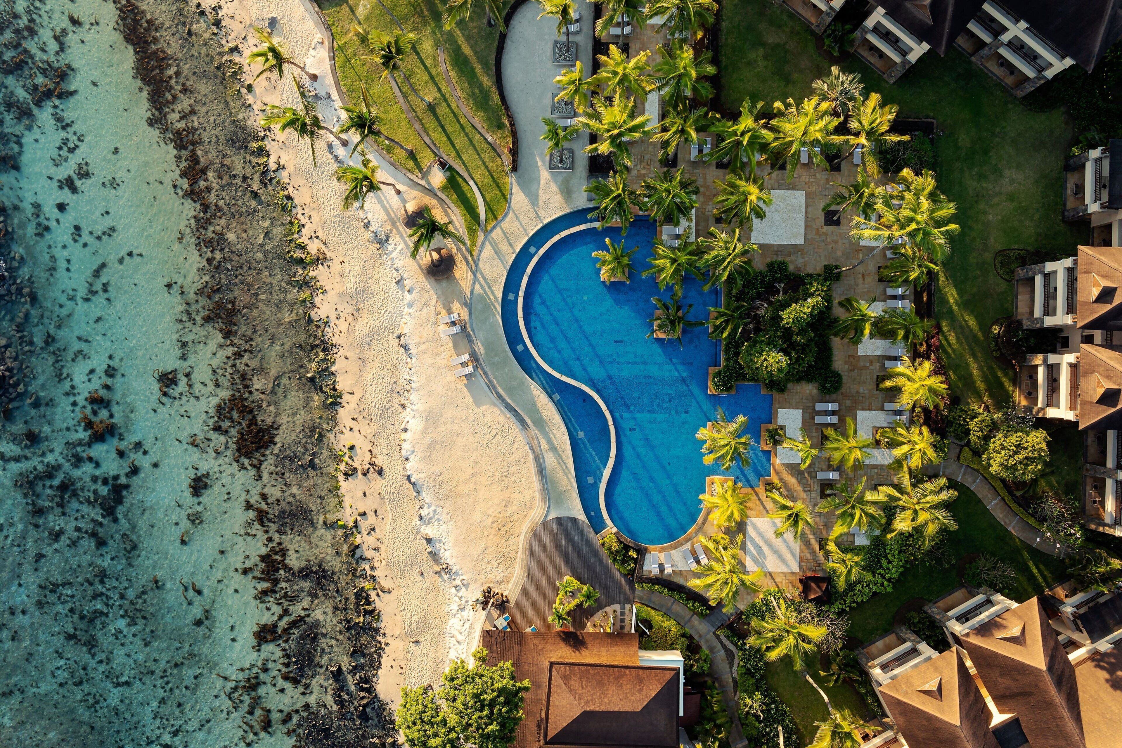 An aerial view of a resort with a swimming pool, beachfront, and palm trees.