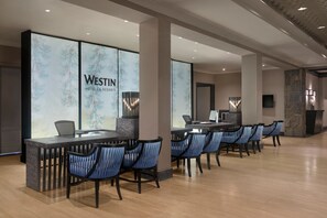 A reception area with a marble wall displaying the Westin Hotels & Resorts logo, a reception desk, and several blue chairs arranged in front of it.