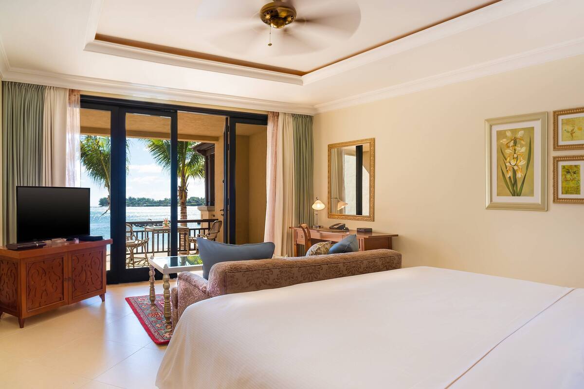 Quarto de hotel com cama, televisão, escrivaninha e vista para o oceano.