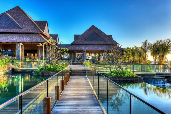 A resort with a wooden boardwalk over a pool, connected to buildings with a triangular roof.